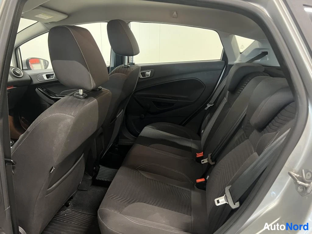 Muu: Auton takaistuimet kuvattu avoimen takaoven kautta; tummat kangasistuimet ja ISOFIX-merkit hihnoissa.
