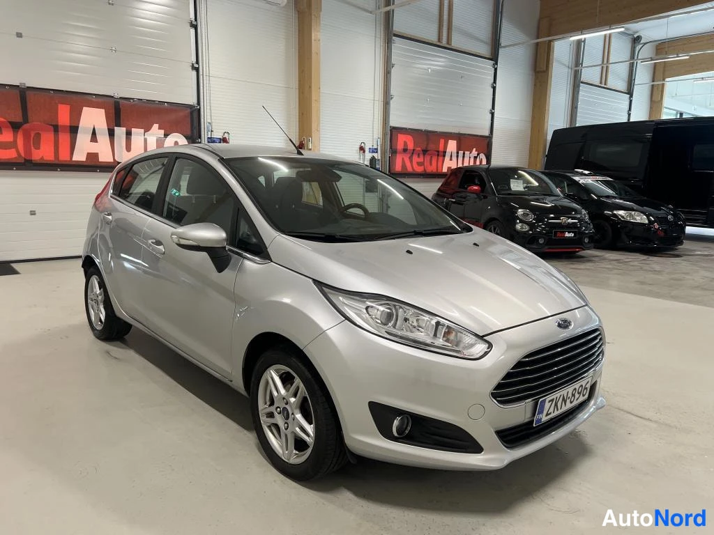 Etuviisto, nokka oikealle: Ford Fiesta -auton etukulma kuvattuna autotallissa, rekisterikilpi, hopeanvärinen korirakennne