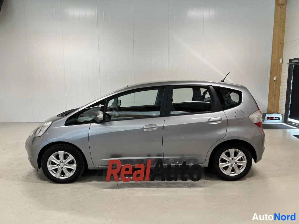 Etuviisto, nokka vasemmalle: Hopeanvärinen Honda Jazz lähes sivusuunnasta, keulan etupyörä ja ajovalo näkyvät vasemmalla.