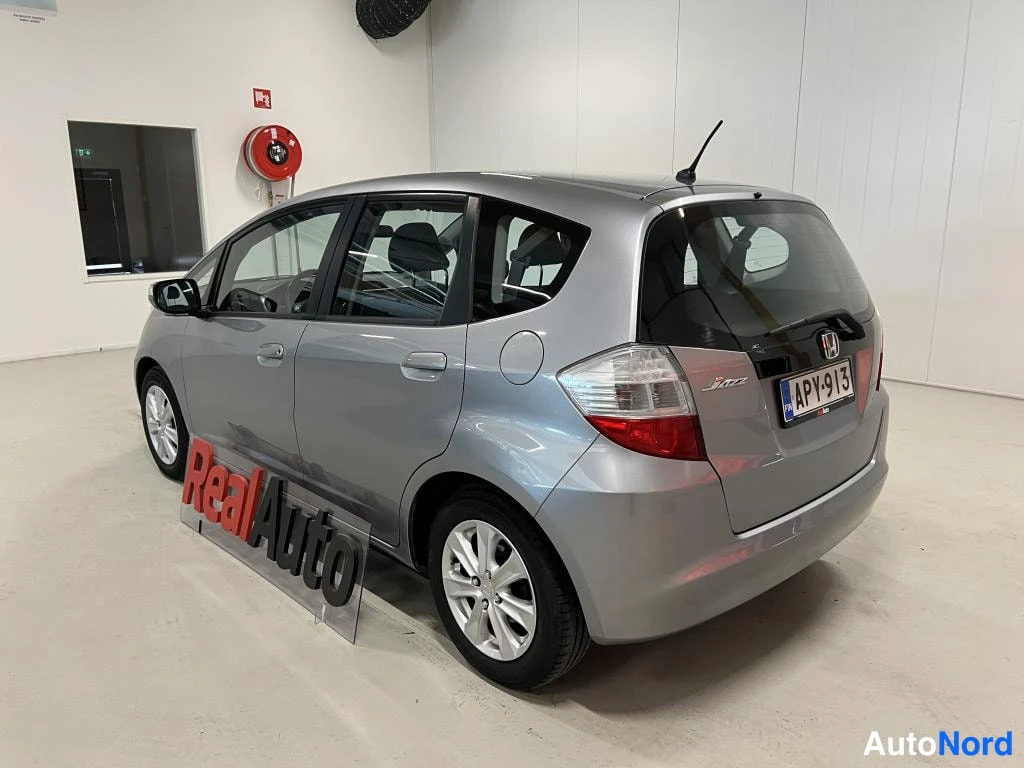 Takaviisto: Hopeanvärinen Honda Jazz taka viistosta vasemmalta, rekisterikilpi, takapuskasta ja kyljestä näkyvät.