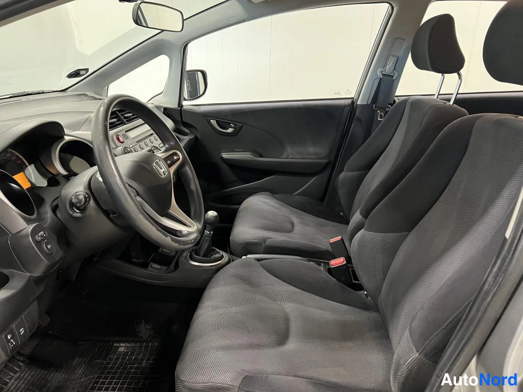 Muu: Honda Jazzin sisätilat: kuljettajan puolen istuin, ohjauspyörä ja manuaalivaihteen vaihtekahva, tummat kangasistuimet.