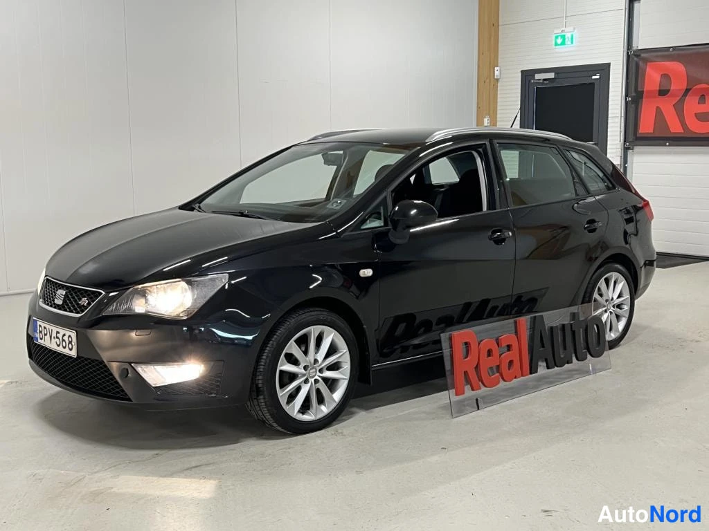 Etuviisto, nokka vasemmalle: Musta Seat Ibiza ST farmari etukulmasta vasemmalta, kylki ja keul näkyvissä, hopeat kevytmetallivanteet, kilpi.