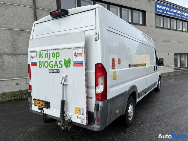 Takaviisto: Valkoisen pakettiauton takaosa ja kylki vinosti takaa kuvattuna, takaluukussa teksti 'Ik rij op BIOGAS' ja nostolaite.