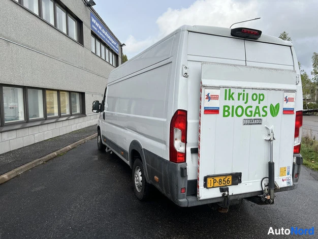 Takaviisto: Valkoisen pakettiauton takaosa ja vasen kylki vinosti takaa kuvattuna rakennuksen vieressä, takaluukussa teksti 'Ik rij op BIOGAS'.