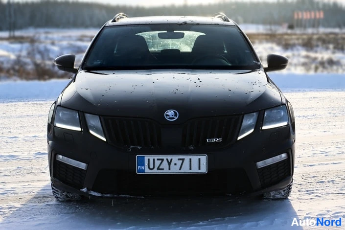 Edestä: Etunäkymä mustasta autosta, rekisteritunnus, lumisella pihalla.
