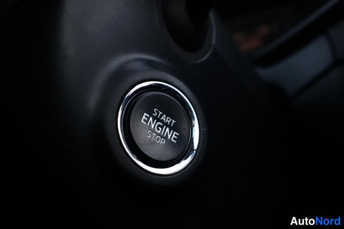Yksityiskohta: Sisätilakuvan tarkennus: musta käynnistyspainike, jossa lukee START ENGINE STOP, hopeareunustettuna tummassa kojelaudassa.