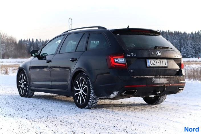 Takaviisto: Musta farmariauto takaviistosta lumisessa ympäristössä, takana Skoda-merkki ja rekisteritunnus.