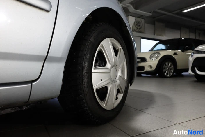 Sivulta: Hopeanvärinen auto lähikuvassa, etupyörä ja kylkipaneeli näkyvät sisätiloissa.