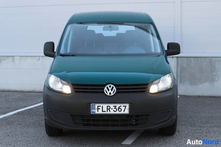Edestä: Volkswagen Caddyn etupää suoraan edestä, vihreä kori, ajovalot päällä, rekisterikilpi.