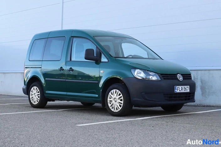 Etuviisto, nokka oikealle: Volkswagen Caddy etuviistosta oikealle parkkitilassa, tummanvihreä kori, rekisterikilpi.