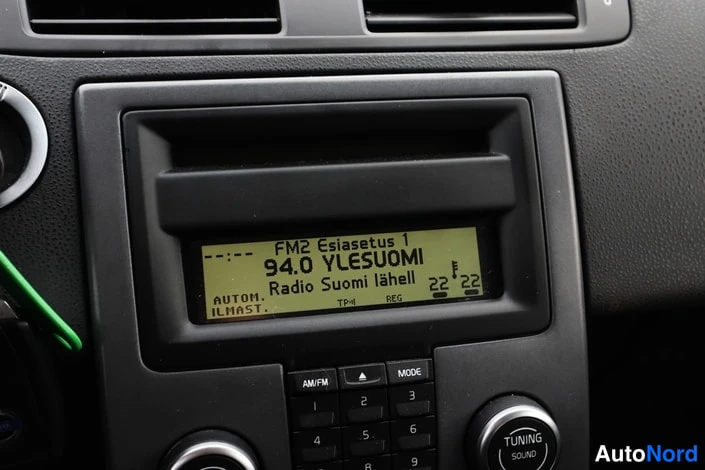 Edestä: Sisäkuva: auton radion näyttö, jossa lukee 'FM2 Esiasetus 1', '94.0 YLESUOMI' ja 'Radio Suomi lähellä', alla AM/FM-, MODE- ja TUNING SOUND -painikkeet.