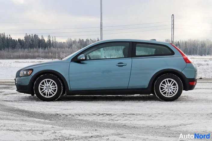 Sivulta: Sinivihreä kaksiovinen henkilöauto sivusuunnasta nokka vasemmalla, paksu lumikerros maassa.