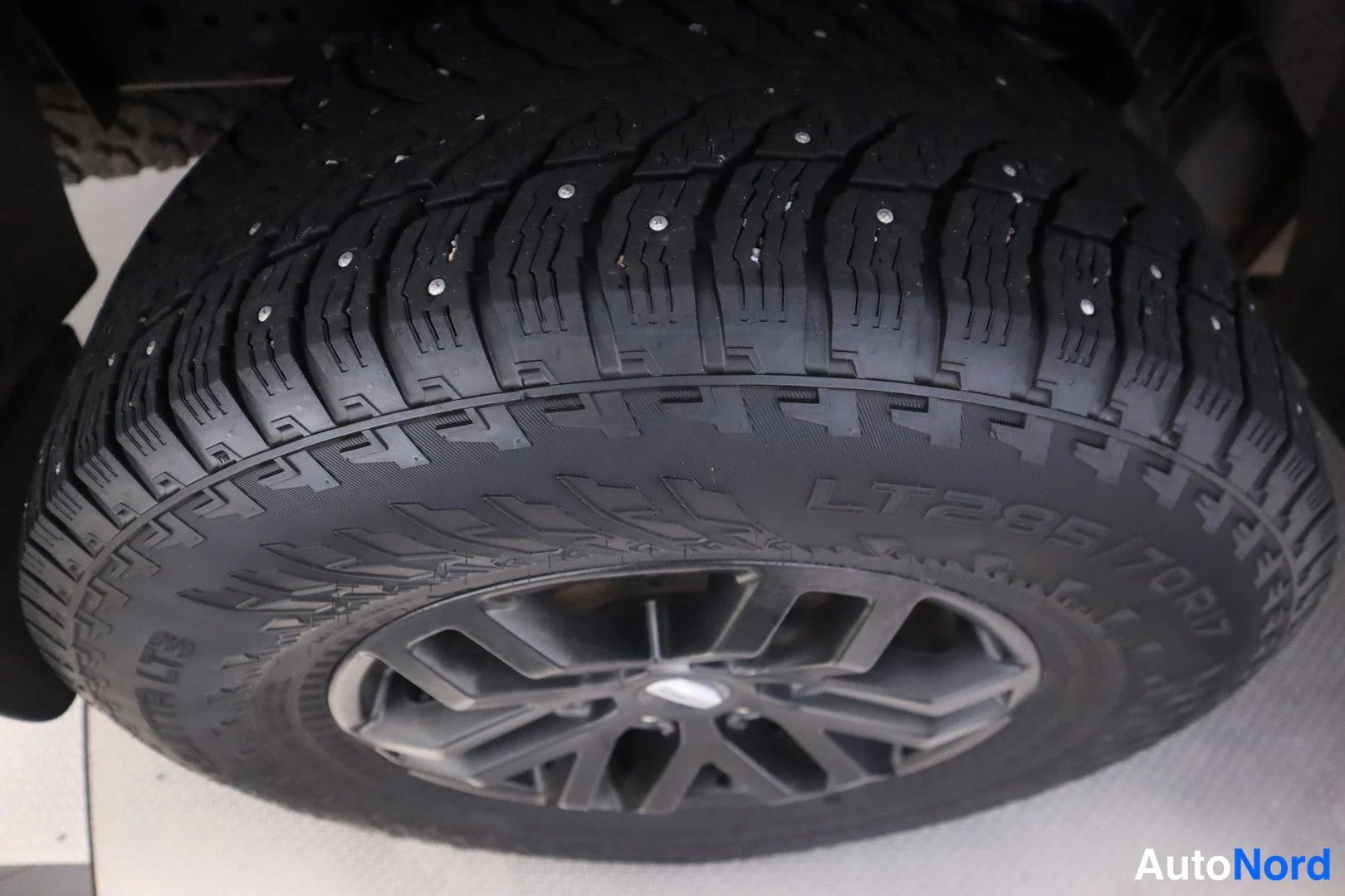 Yksityiskohta: Lähikuva nastarenkaasta; renkaan kyljessä koko LT285/70R17 ja tumma kevytmetallivanne.