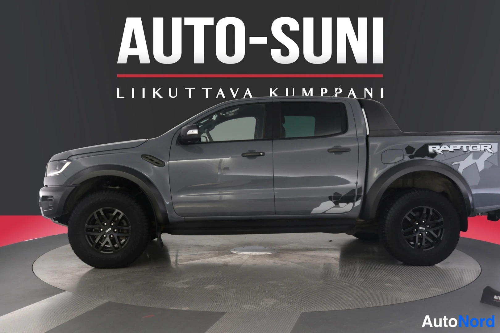 Etuviisto, nokka vasemmalle: Harmaan Ford Ranger -mallin sivukulma hallissa, AUTO-SUNI-taustalogotyyppi.