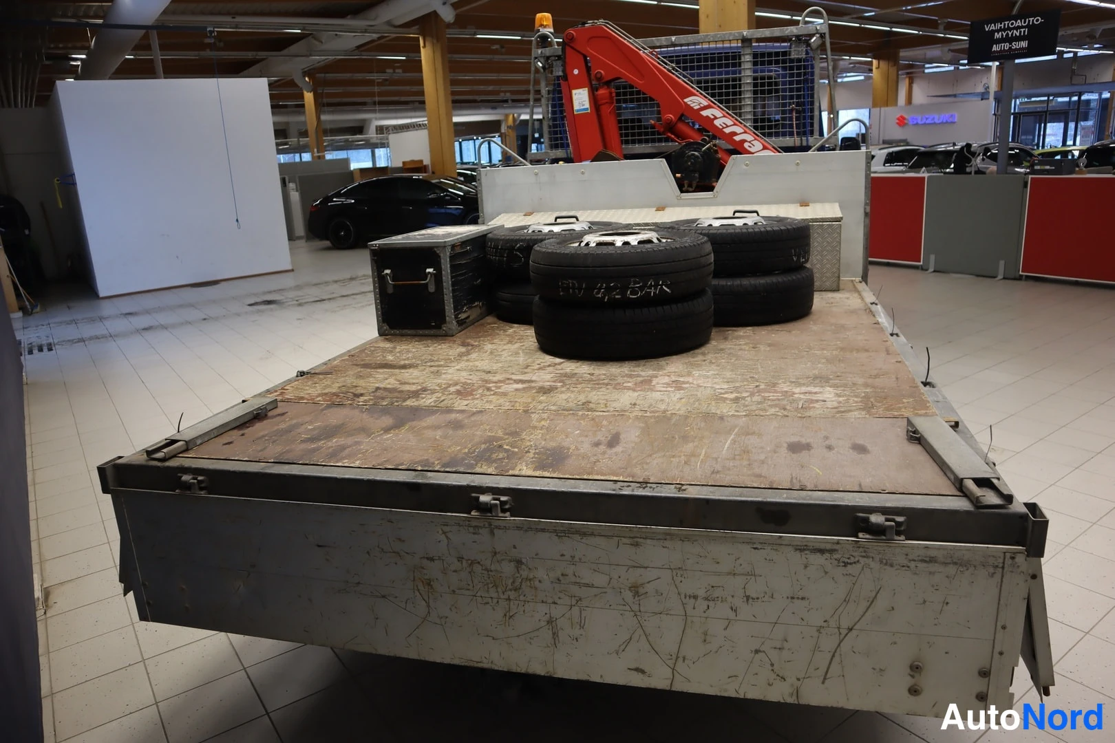Muu: Kuorma-auton lavan kulma kuvattuna ylhäältä; lavalla pinoa renkaita, muovinen varustelaatikko ja punainen Fassi-nosturi lavan päässä.