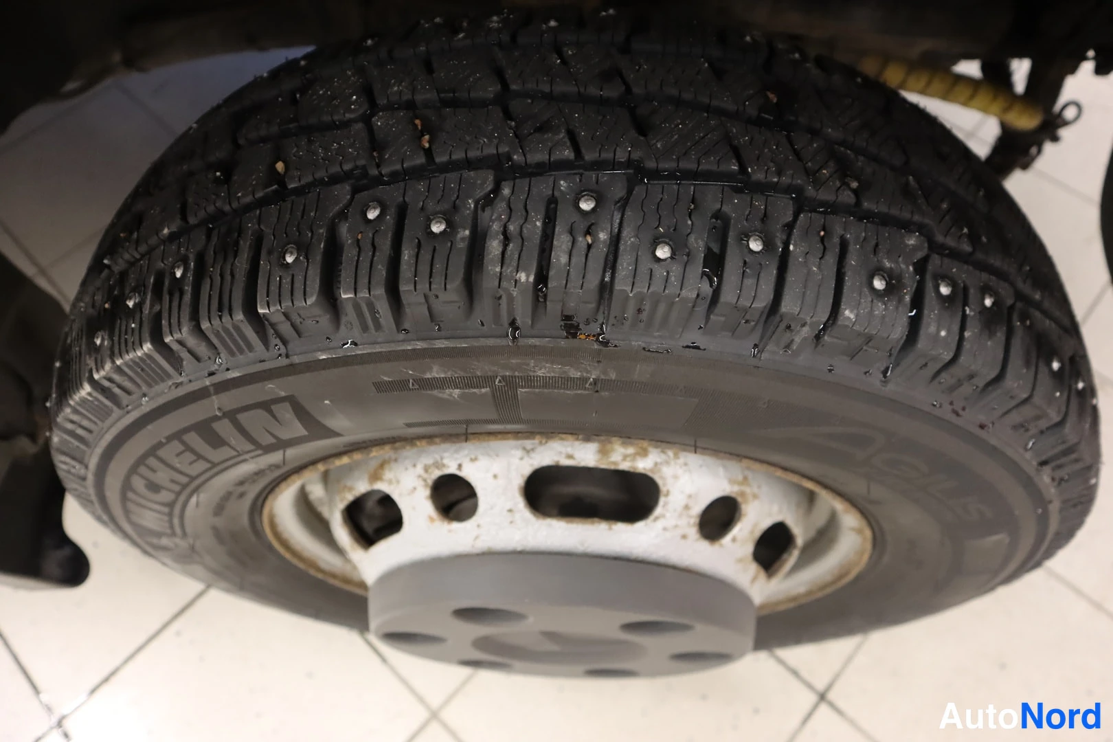 Muu: Lähikuva Michelin-nastarenkaasta ruosteisella teräsvanteella, nastat näkyvät kulutuspinnassa.