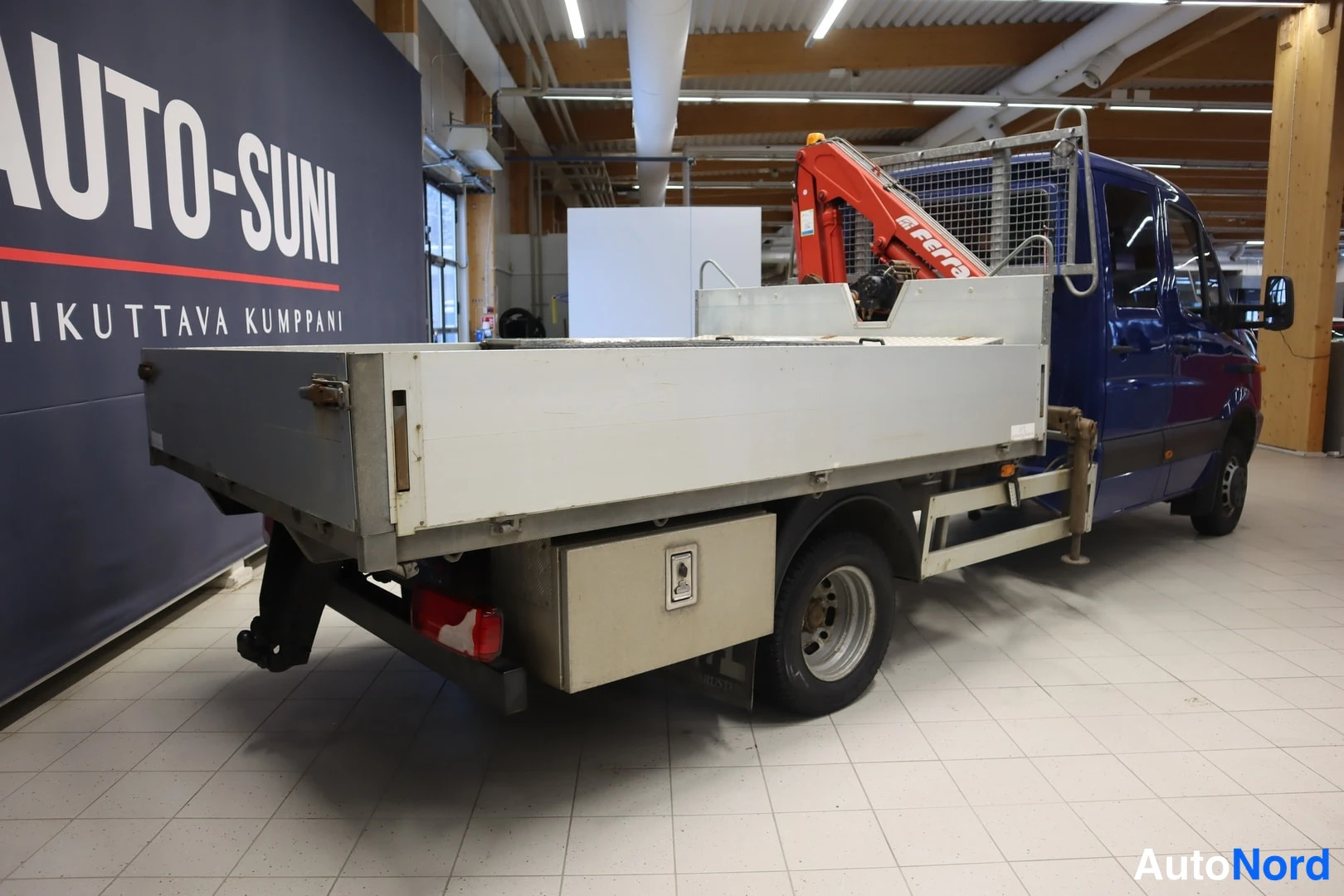 Takaviisto: Rear three-quarter view of the blue truck showing the flatbed and folded red crane.