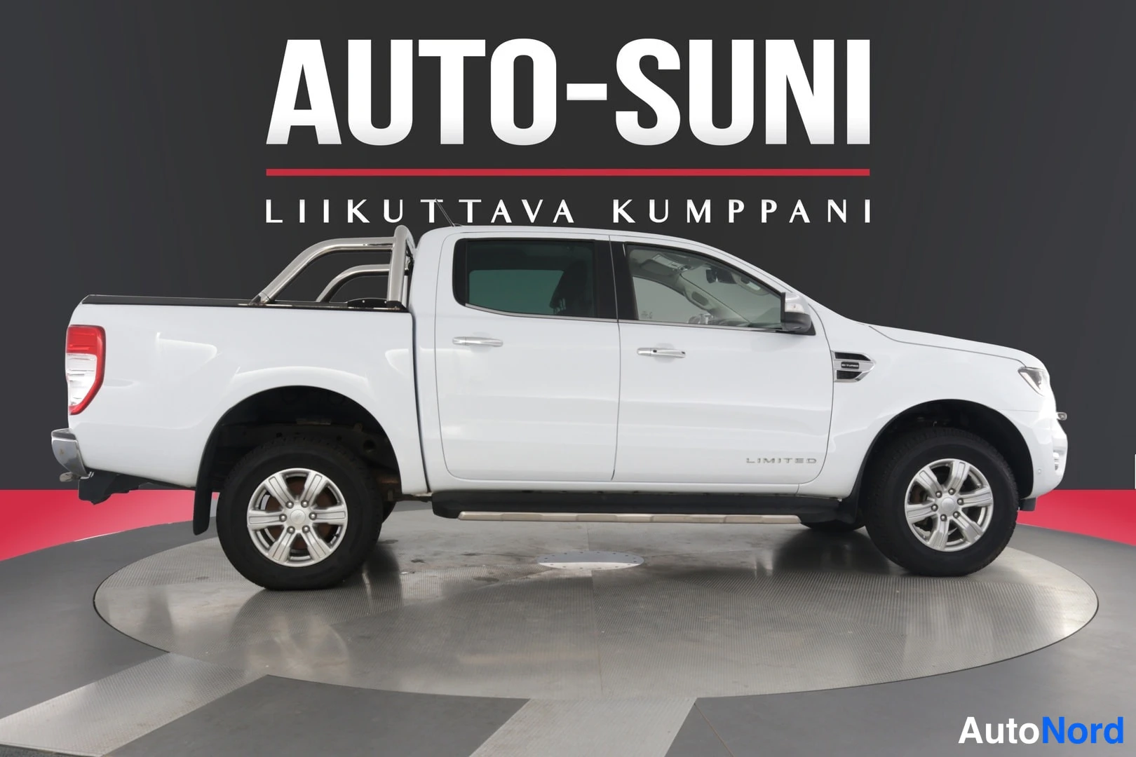 Sivulta: Valkoinen Ford Ranger Limited -näkymä, jossa näkyy oikea puoli ja takapää. Autossa on metalliset sisustanjalusta-kiinnikkeet, renkaat ja kansi. Taustalla on mus