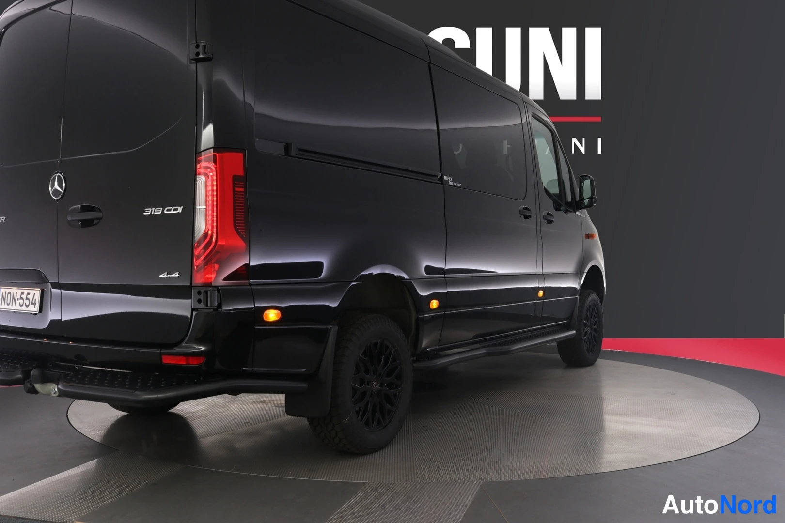 Takaviisto: Musta Mercedes-Benz Sprinter -pakettiauto takaa kolmanneksesta oikealta, takavalo ja perävaunun vetokoukku näkyvät.