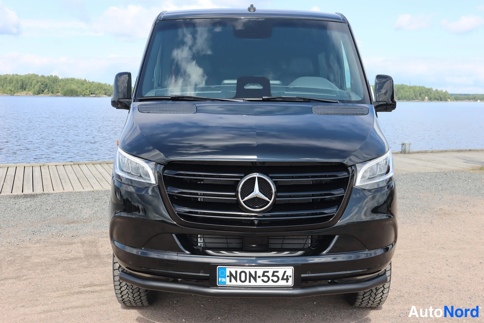 Edestä: Musta Mercedes-Benz Sprinter -pakettiauto suoraan edestä kuvattuna, etupansseri ja rekisterikilpi N0N-554 näkyvät.