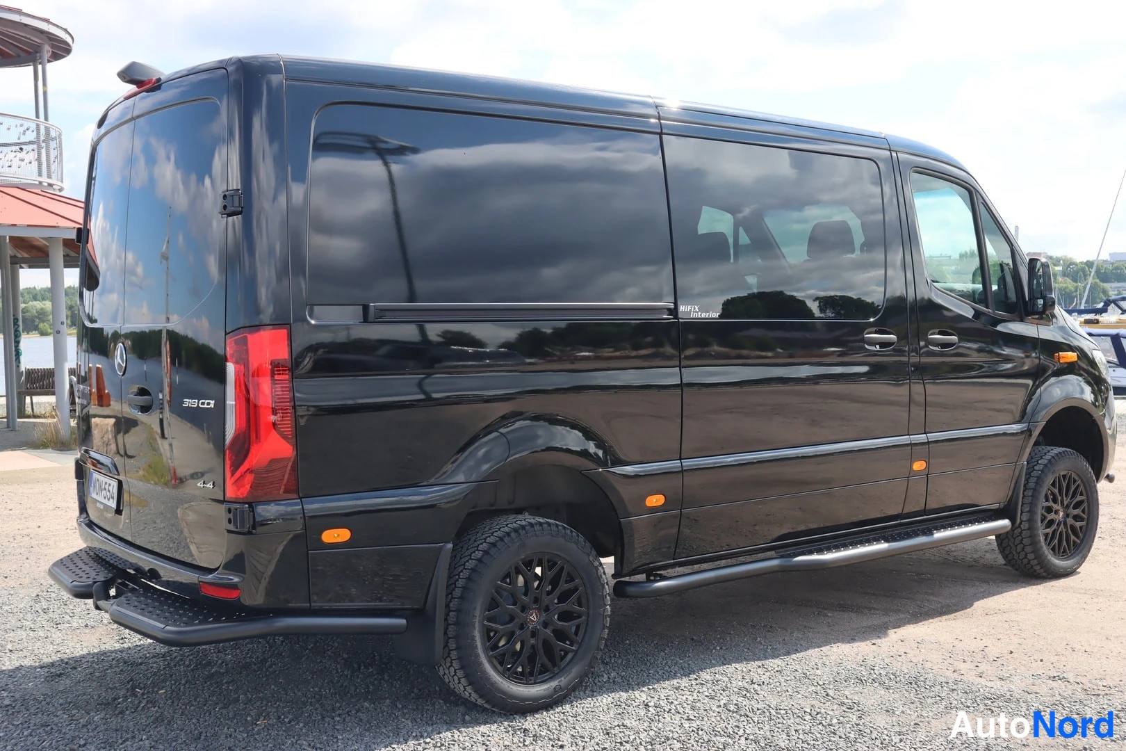 Takaviisto: Musta Mercedes-Benz Sprinter -pakettiauto takaa-suunnasta oikeasta kulmasta kuvattuna, kyljetapit ja tummat kevytmetallivanteet näkyvät.