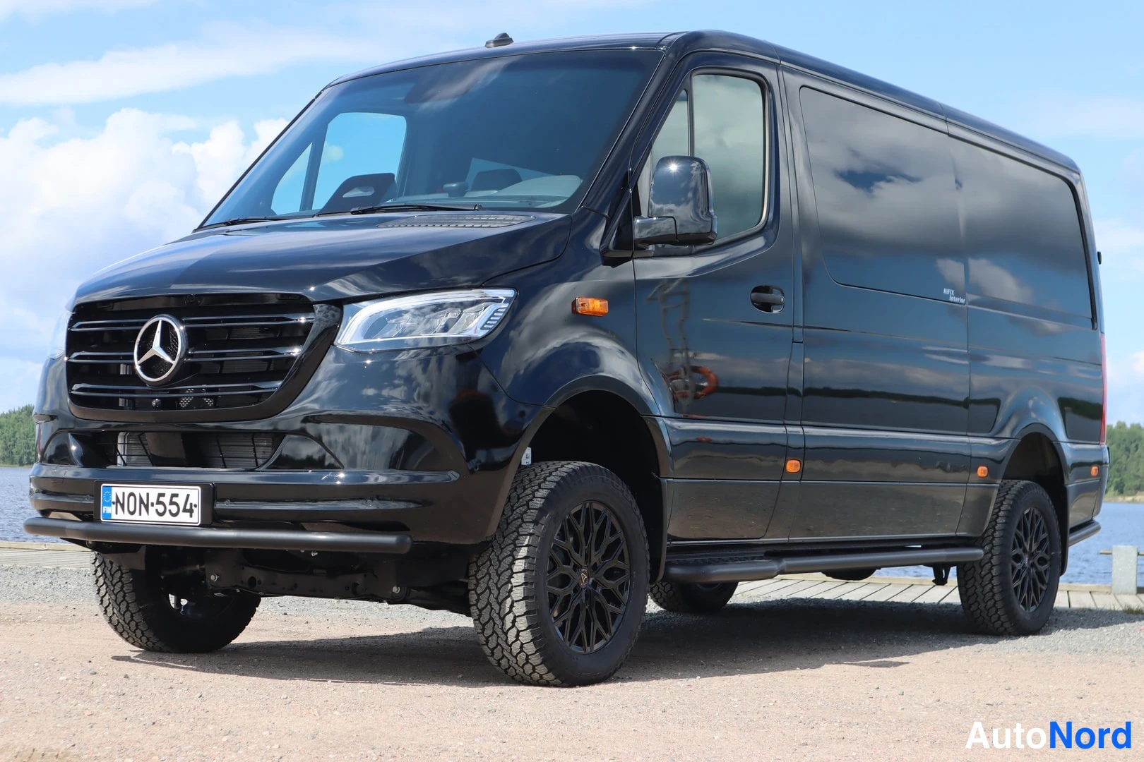Etuviisto, nokka vasemmalle: Musta Mercedes-Benz Sprinter -pakettiauto edestä-suunnasta vasemmasta kulmasta kuvattuna, musta etusäleikkö ja täysi-LED-ajovalot, rekisterikilpi.