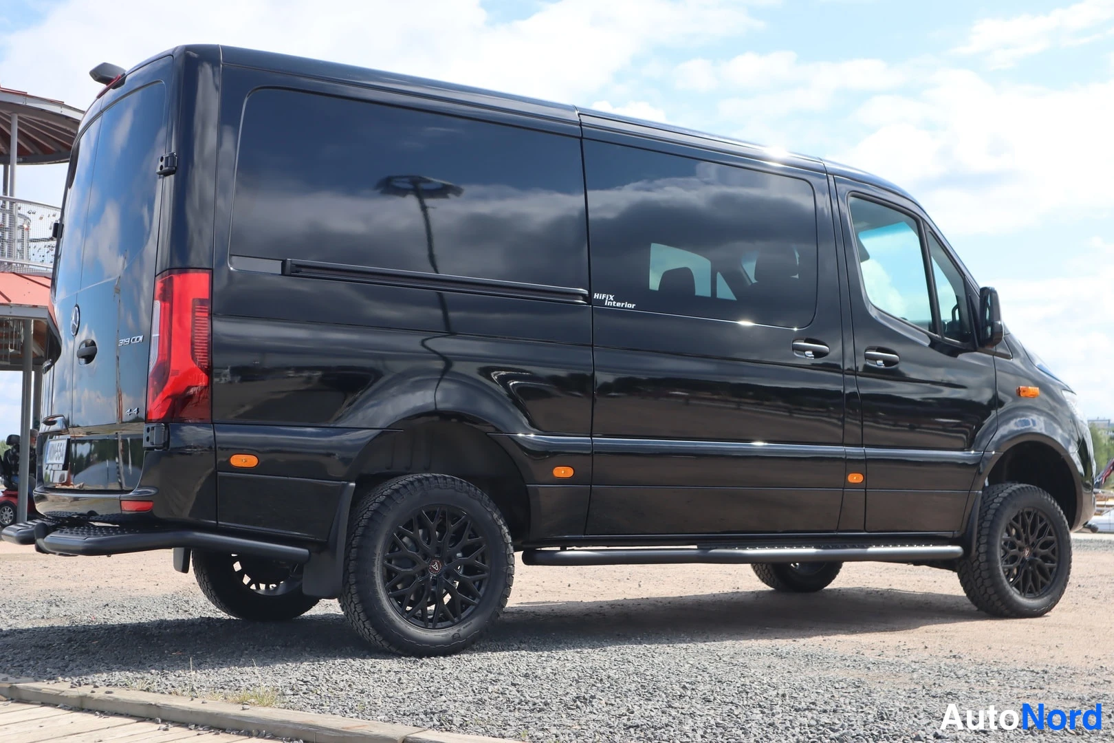 Takaviisto: Musta Mercedes-Benz Sprinter -pakettiauto takaa kulmasta kuvattuna, tummat vanteet.