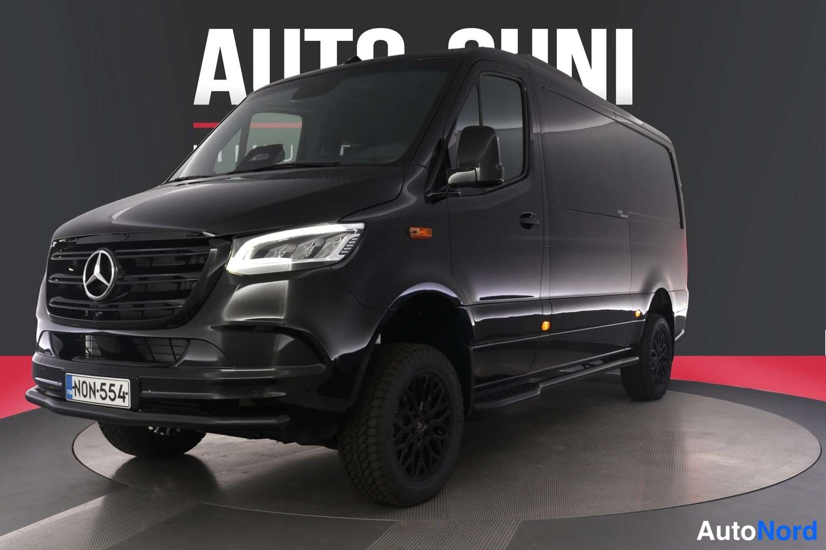 Etuviisto, nokka vasemmalle: Musta Mercedes-Benz Sprinter etuviistöstä kuvattuna showroomissa, keulalla Mercedes-tähti ja rekisterikilpi.