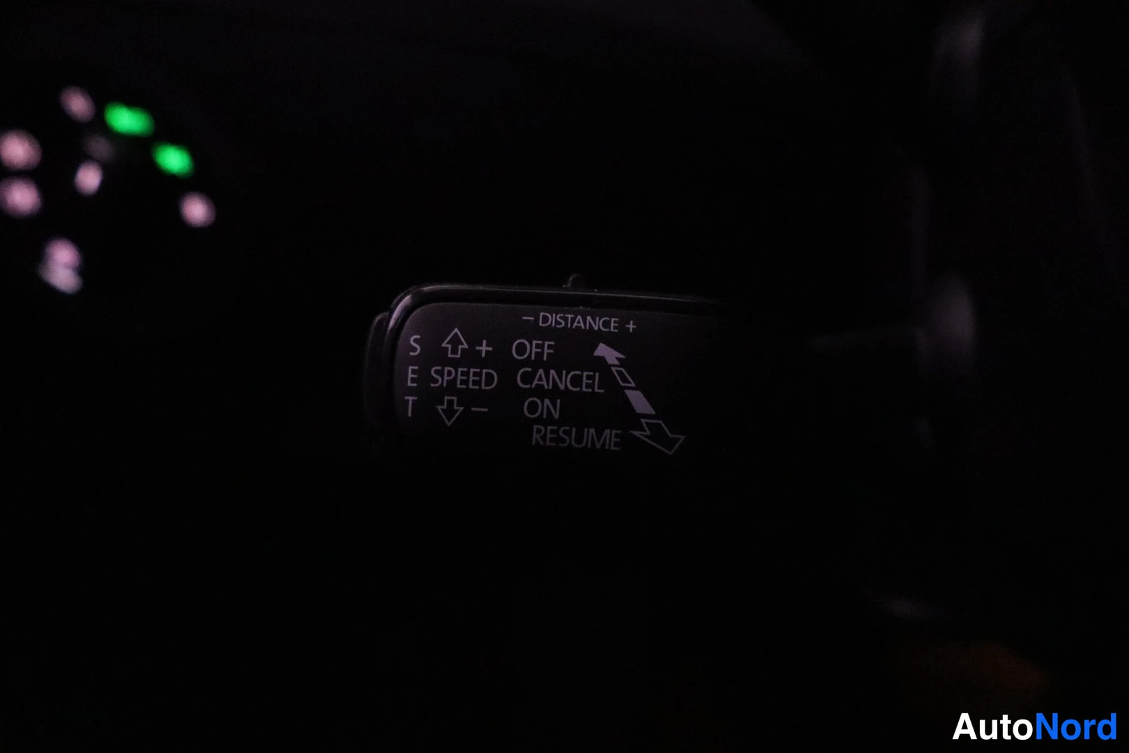 Ohjaamo: A close-up view of the turn signal stalk illuminated against a dark background, showing text labels for CRUISE_CONTROL functions such as SET SPEED and RESUME.