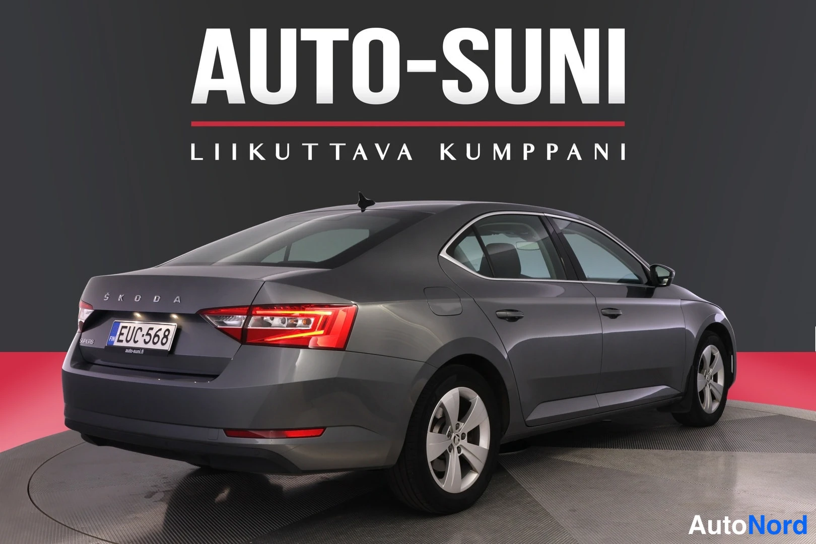Takaviisto: Autoteen takakulmanäkymä vasemmalta: harmaan Škoda Superb -sedan takavalovalo ja rekisteritunnus, tavaratilan kannessa ŠKODA-teksti.