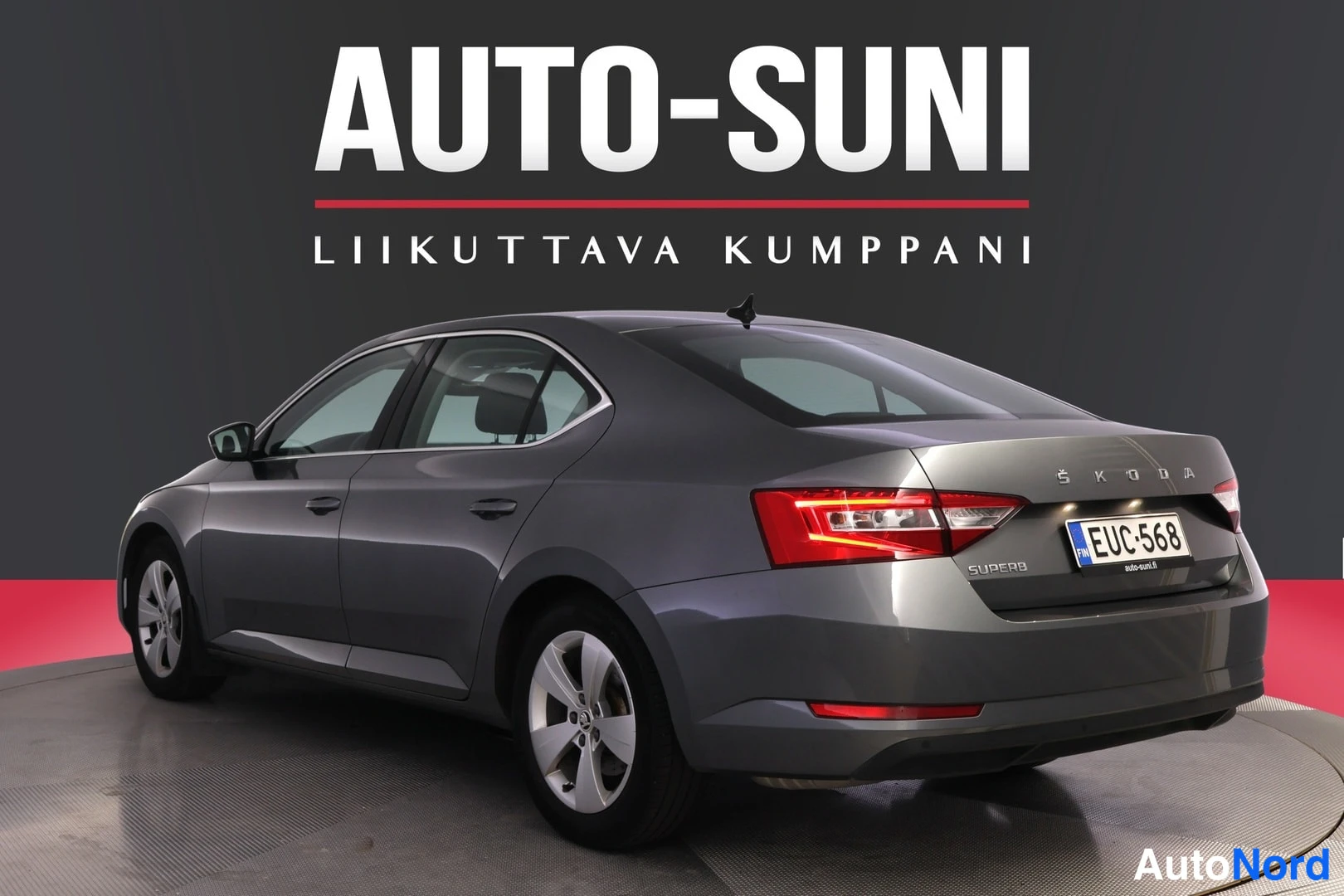 Takaviisto: Autoteen takakulmanäkymä vasemmalta: harmaan Škoda Superb -sedan takavalo ja rekisteritunnus, tavaratilan kannessa tekstit ŠKODA ja SUPERB.