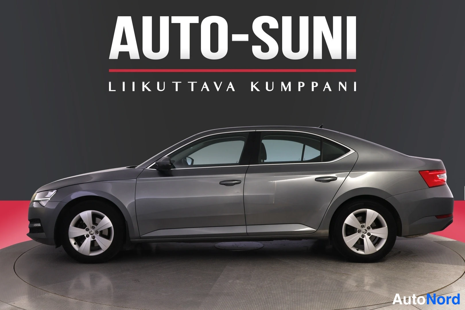 Sivulta: Auton kylki ja etuosa hieman vinosti kuvattuna, harmaa sedan.