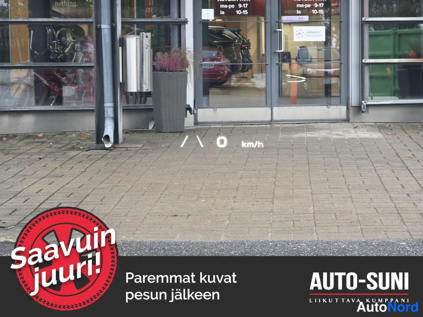Muu: Näkymä auton tuulilasin läpi kaupan oveen, tuulilasiin heijastuu heads-up-näytön lukema 0 km/h.