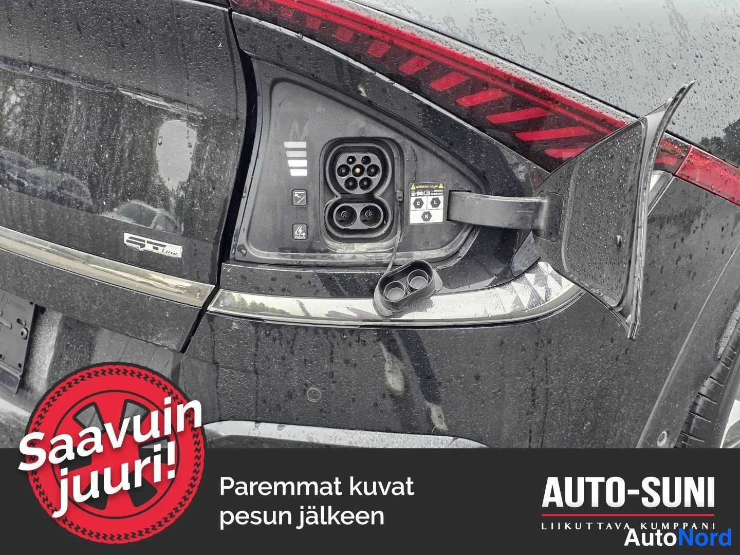 Muu: Lähikuva avoimesta latausluukusta: CCS-tyyppinen latausportti, sulakekortti ja RT-sertifikaattitarra näkyvissä, koripinta märkä.
