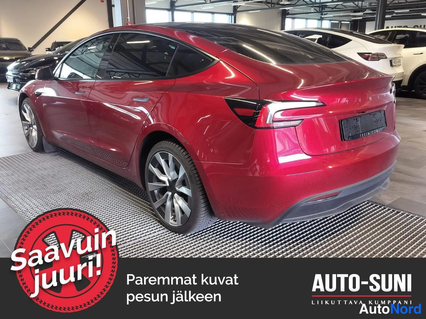 Takaviisto: Punainen Tesla Model 3 -henkilöauto takaosa vasemmalta kuvattuna autosalonissa, takavalojen ja TESLA-tekstin näkyvissä.