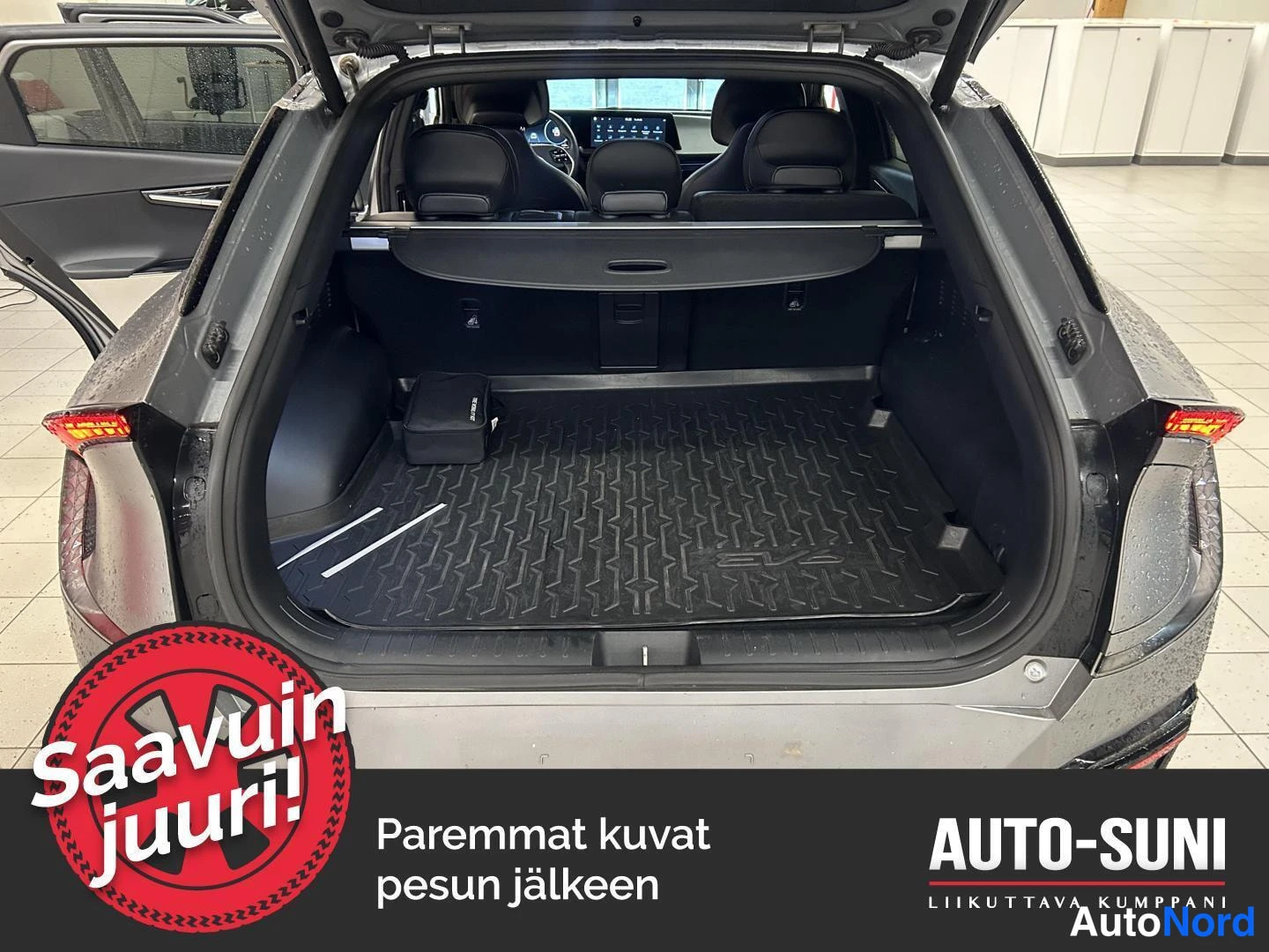 Takaa: Auki pidetty takaluukku ja avattu tavaratila: tumma muovimatto, varashelfi ylhäällä ja takaistuinten selkänojat näkyvissä auton takaa kuvattuna.