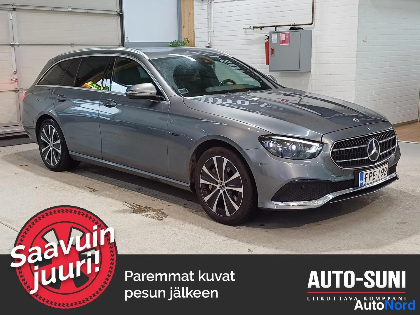 Etuviisto, nokka oikealle: Hopeanharmaa Mercedes-Benz E-farmari kuvattuna kulmassa edestä oikealta sisätiloissa, rekisterikilpi.