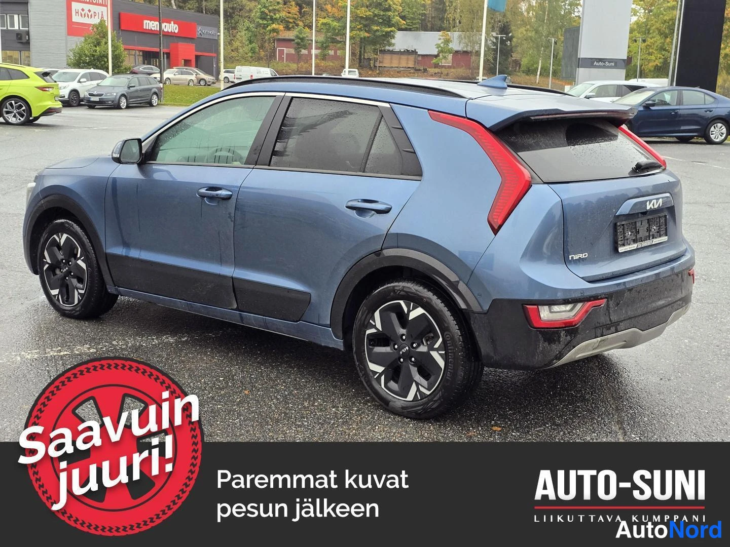 Takaviisto: Sinisen Kia Niro -maasturin taka-sivukulmakulma; perä ja vasen kylki näkyvät märällä parkkialueella.