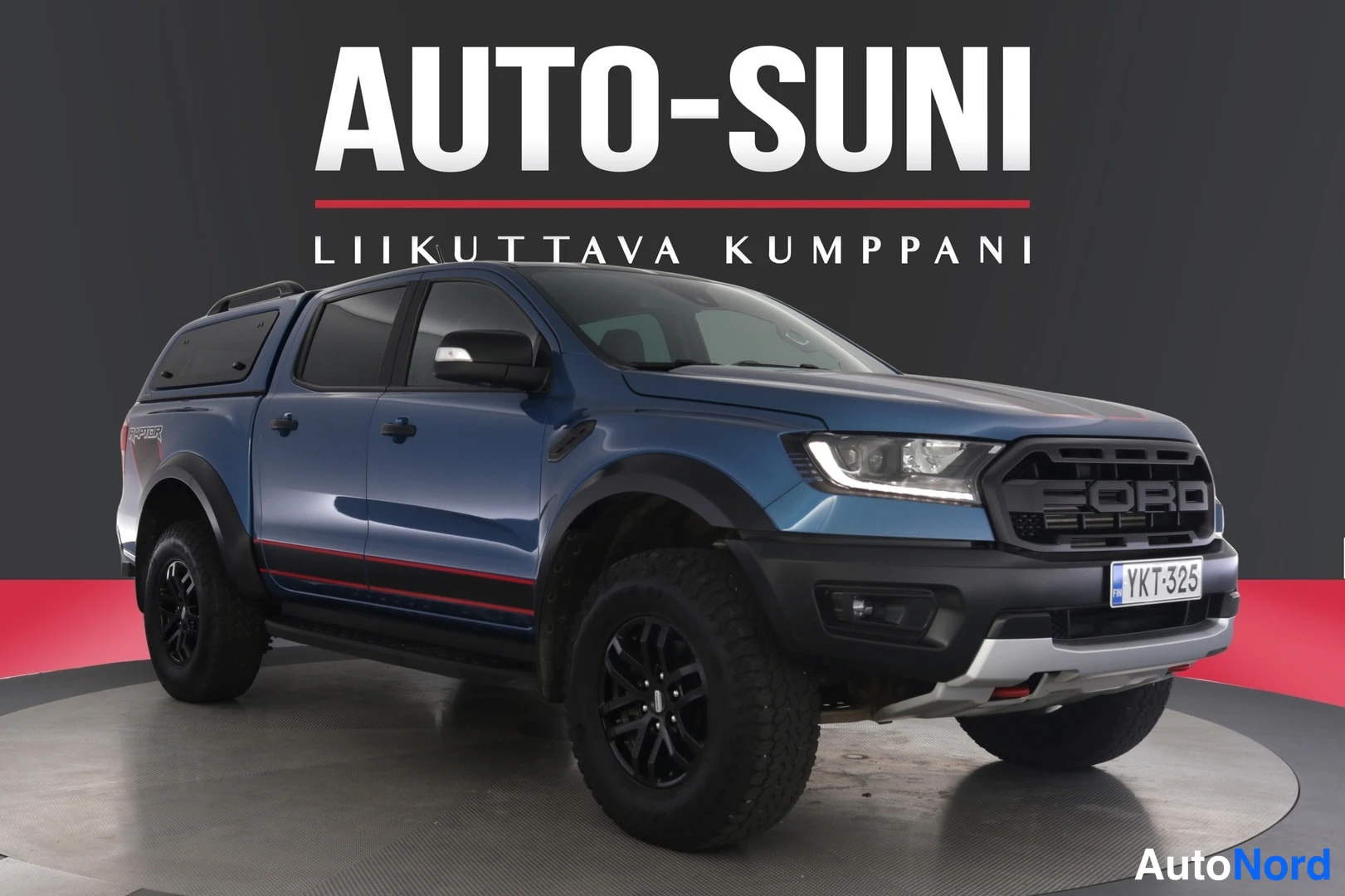 Etuviisto, nokka oikealle: Sininen Ford Ranger -lava-auto nähtynä etuviistosta, tumma tausta ja myyjän mainosgraafiikka.