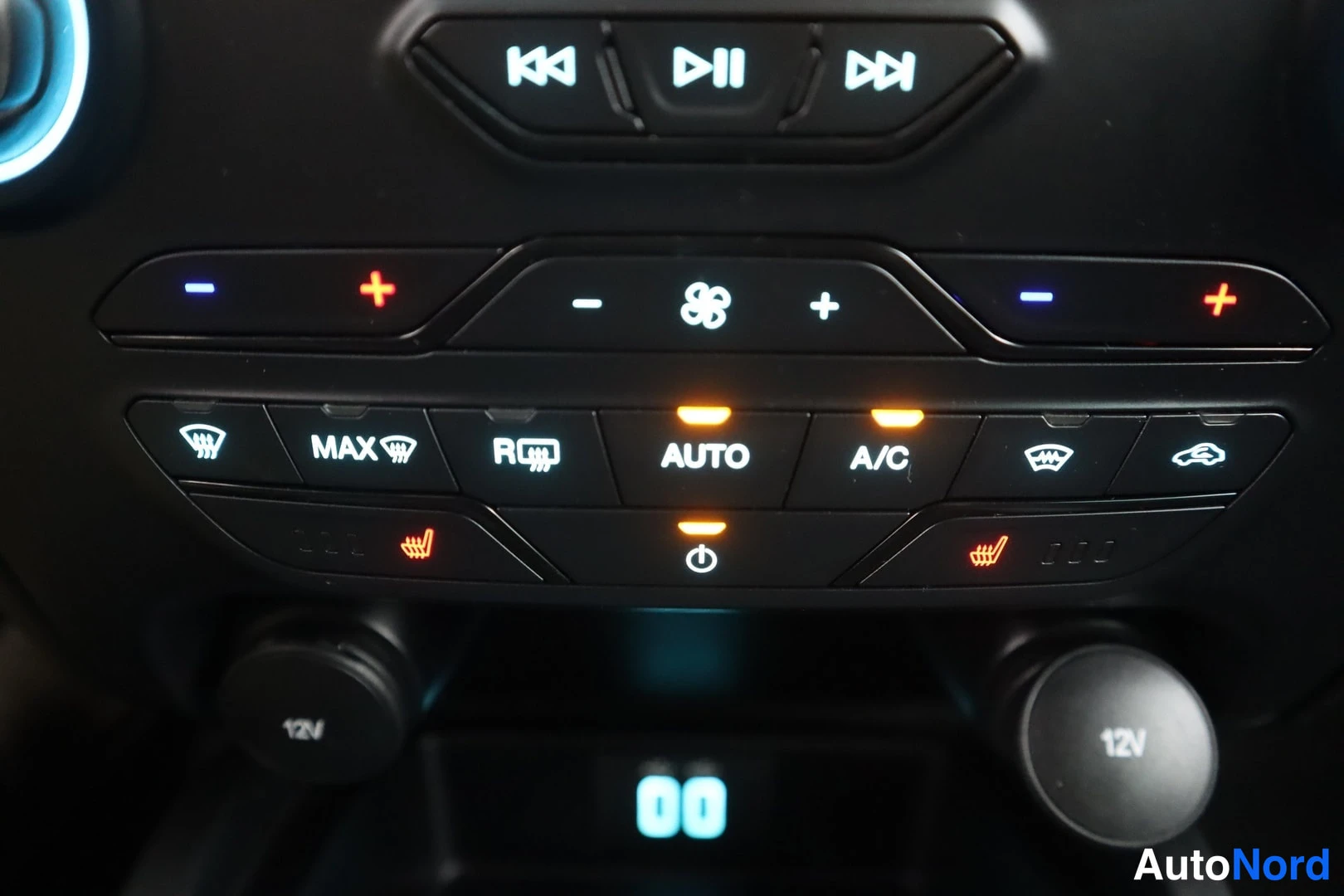 Yksityiskohta: Ilmastointilaitteen ohjauspaneeli: AUTO- ja A/C-napit, MAX-laittostuva ja takalasin lämmitys, oranssit istuinlämmityksen merkkivalot, kaksi 12V-pistorasiaa sekä