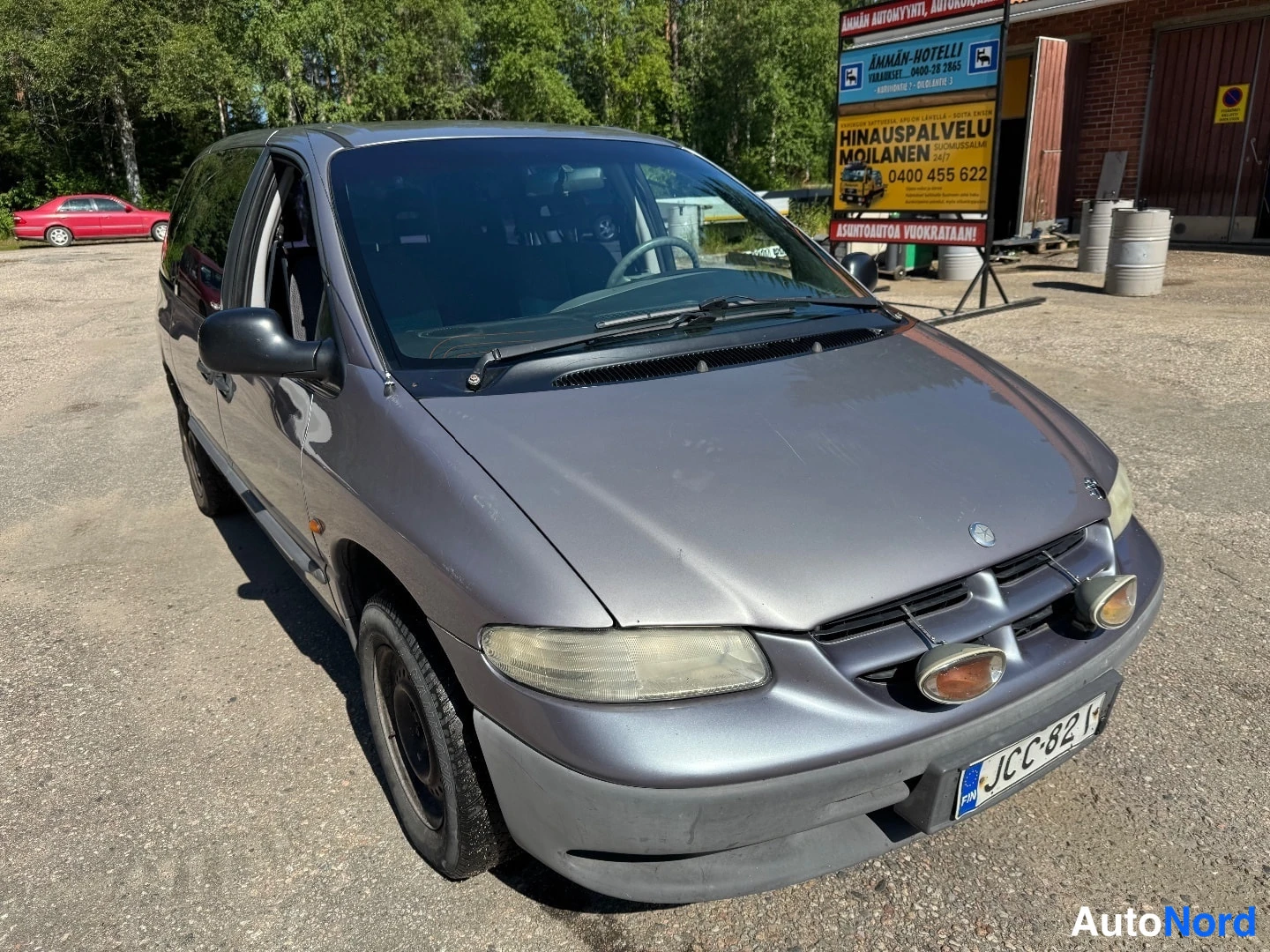 Etuviisto, nokka oikealle: Etu- ja vasen sivunäky kuluneesta harmaasta Chrysler-tavarallisista. Mustat teräkset vanteet. Lisävälintavalot puskurissa.
