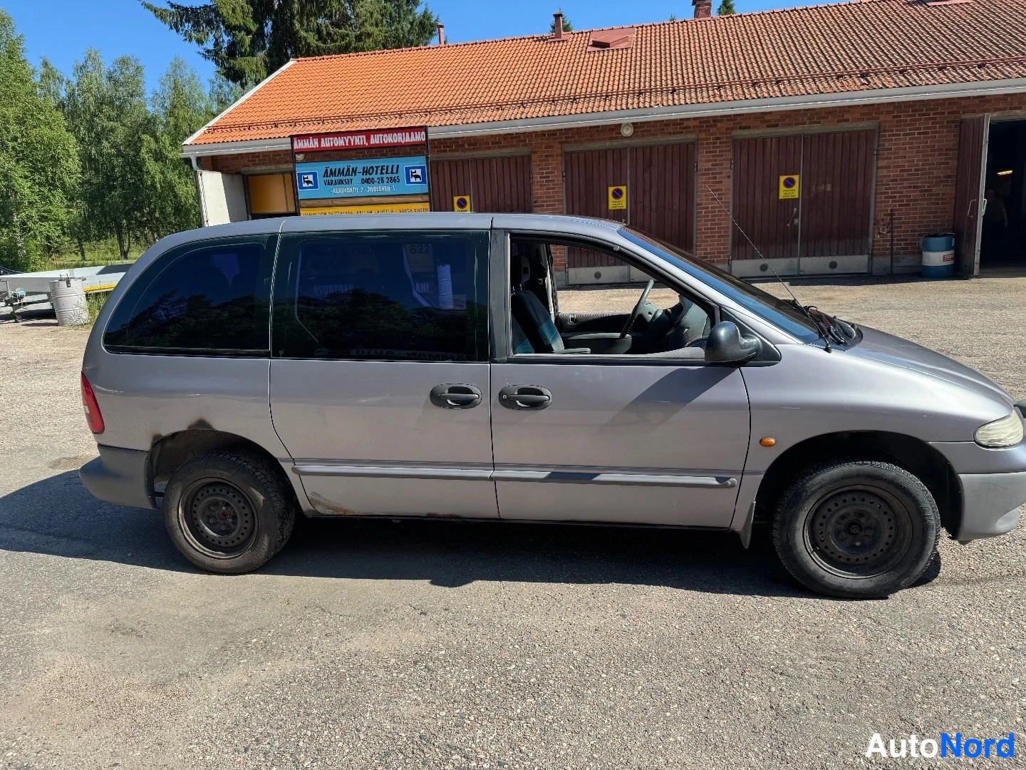 Etuviisto, nokka oikealle: Hopeanharmaa Chrysler Voyager kuvattuna etukulmasta oikealta: auton kylki ja keulan ajovalo näkyvät, ikkunat ovat tummat ja pyörissä mustat teräsvanteet.