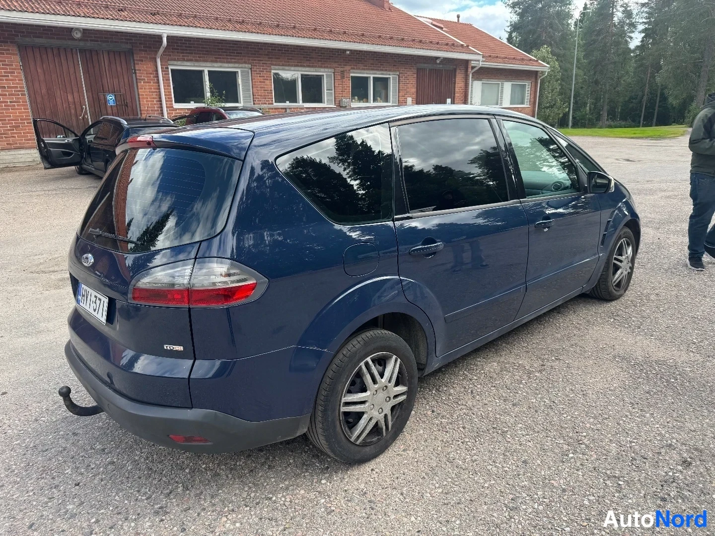 Takaviisto: Takanurkkakuva tummansinisestä tila-autosta: takavalot, takaluukku ja kyljen ovet näkyvät, vetokoukku takapuskurin alla ja rekisterikilpi luettavissa.