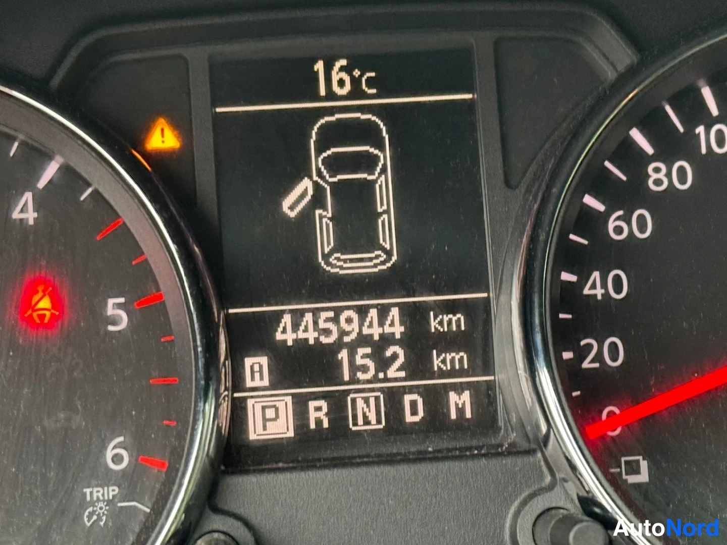 Sivulta: Erittäin läheltä kuvattu mittariston keskinäyttö: lukema 445944 km, 15.2 km, ulkolämpötila 16°C, vaihde P korostettuna sekä avoimen oven symboli.