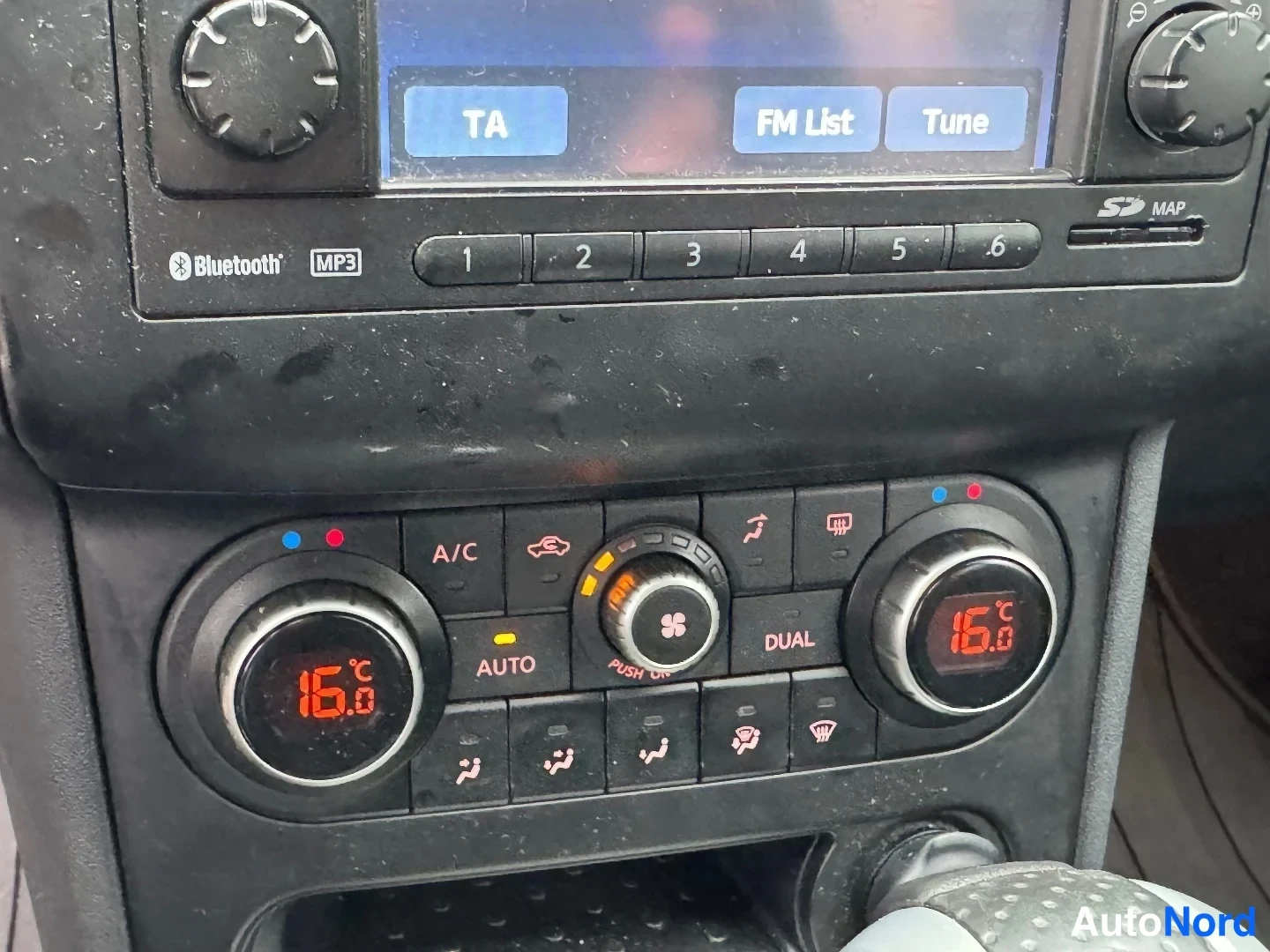 Muu: Auton kojelaudan ilmastointipaneeli ja radion näyttö: kaksivyöhykeilmastointi (A/C, AUTO, DUAL), lämpötila 16,0 °C molemmin puolin, näytöllä TA-, FM List- ja Tu