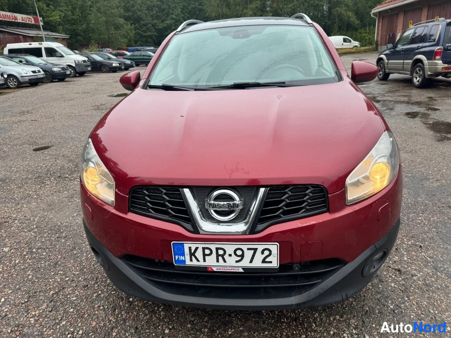 Edestä: Tummanpunaisen henkilöauton keula suoraan edestä päin. Rekisterikilpi, Nissan-merkki ja musta etusäleikkö näkyvät.