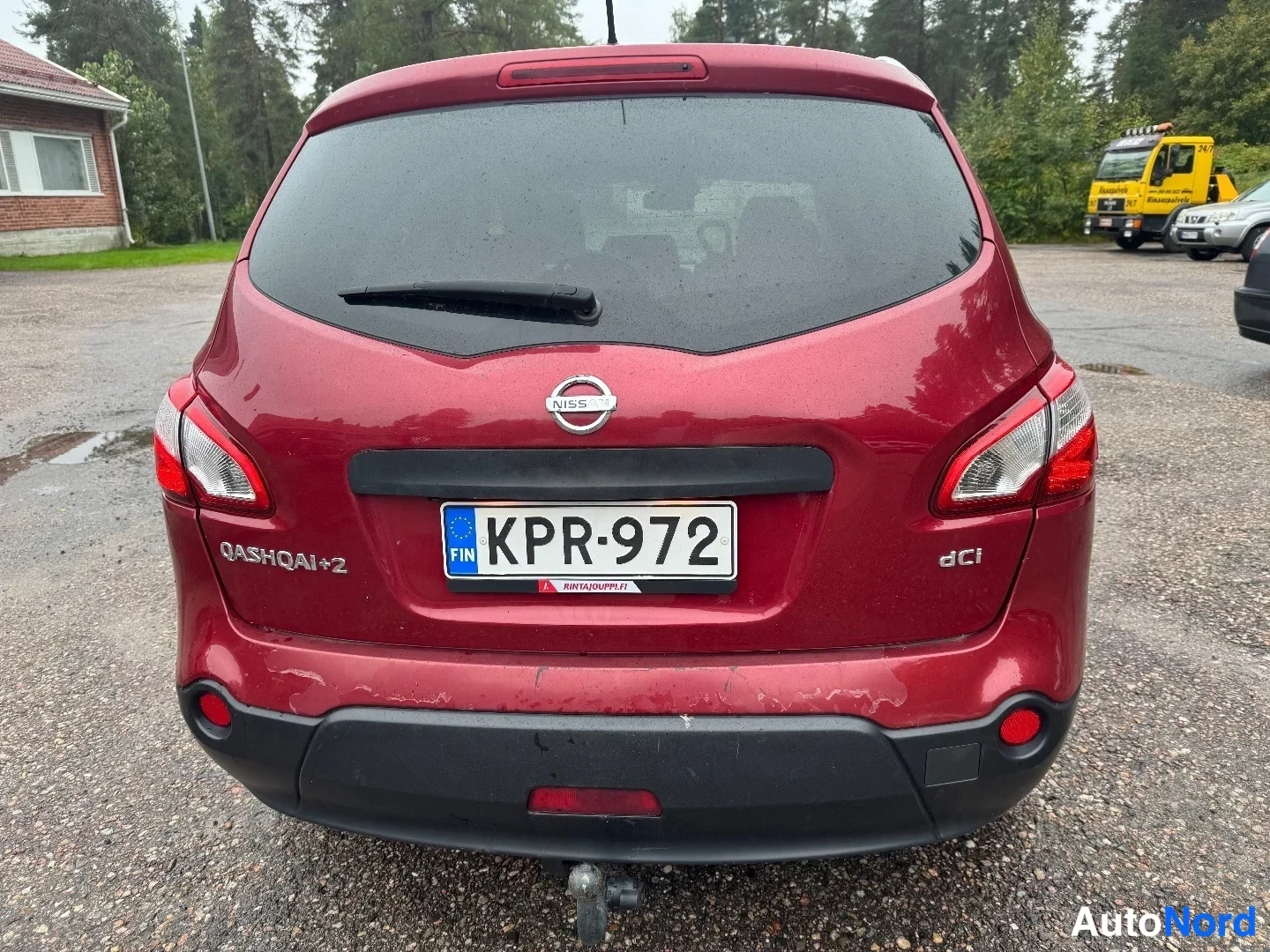 Takaa: Auton takanäkymä suoraan takaa: rekisterikilpi, NISSAN-logo sekä QASHQAI+2- ja dCi-tekstit takaluukussa, takaikkunan pyyhkijä ja vetokoukku puskurin alla.