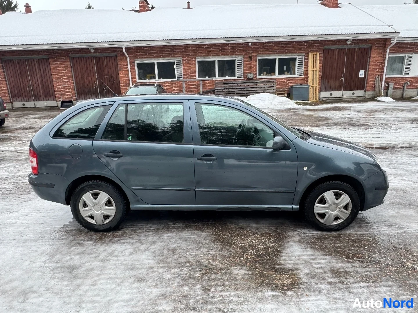 Takaviisto: Harmaa farmarikorinen henkilöauto sivulta takaa kuvattuna lumisella pihalla.