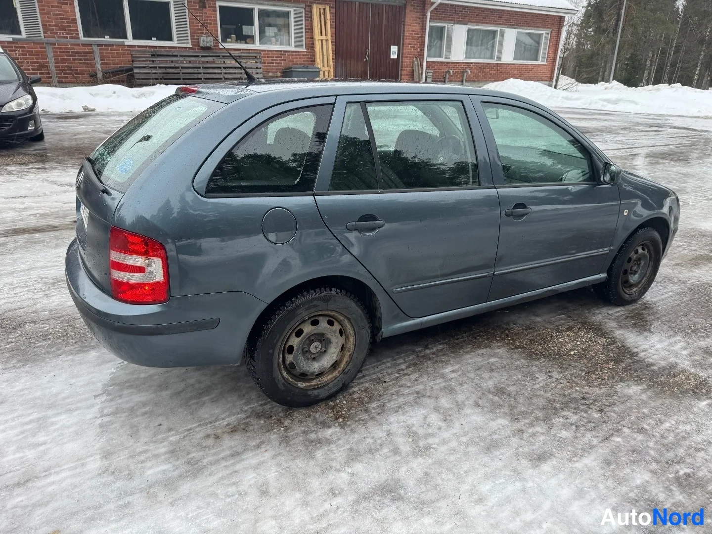 Takaviisto: Harmaansininen farmariauto kuvattuna takakulmasta sivulta lumisella pihalla; takavalo, takaluukku ja koko kylki näkyvät.