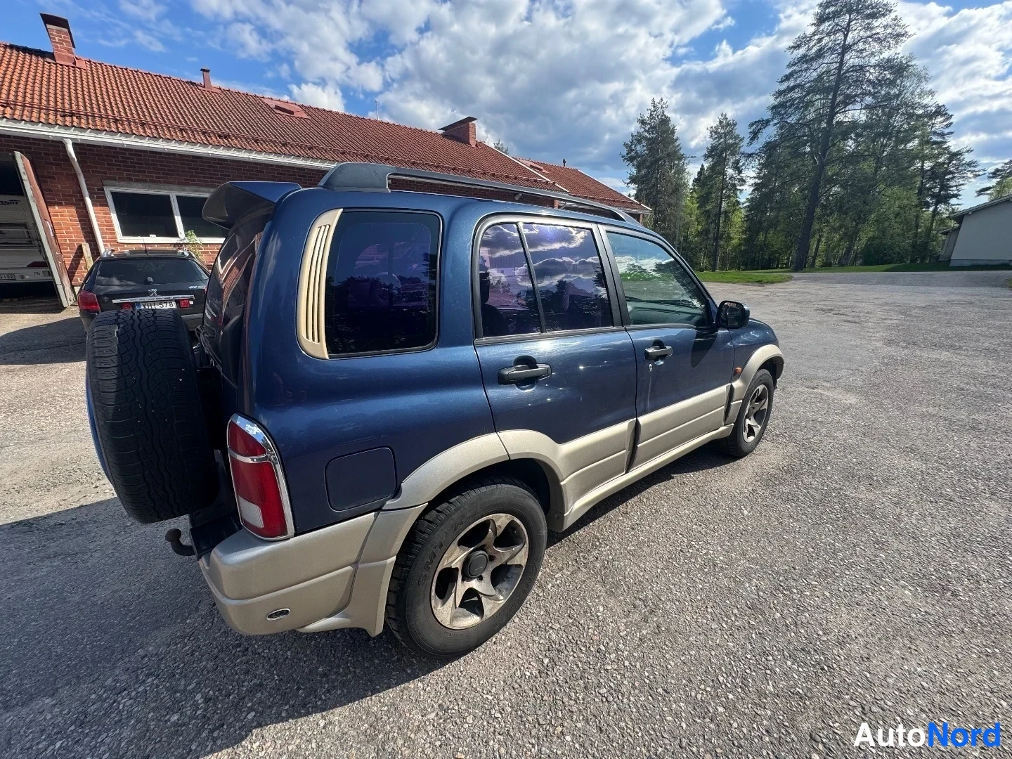 Takaviisto: Tummansininen maasturi kuvattuna takaa sivusuunnasta: varapyörä takaluukun kannella, punavalkoinen takavalo, kattokaiteet ja beigestä muovista tehdyt aluslistat